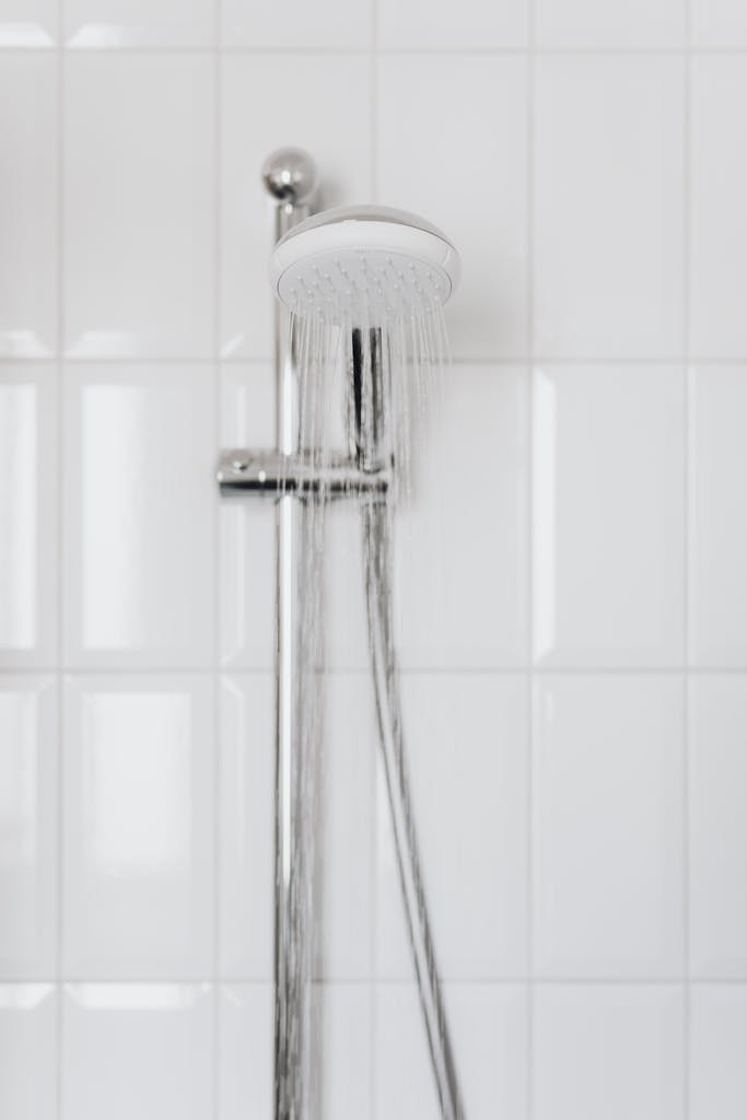 Chrome showerhead with flowing water on white tiled wall, depicting modern bathroom aesthetics.